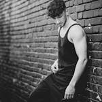 A stylish pose in a black tank top against a brick wall, Tirana.